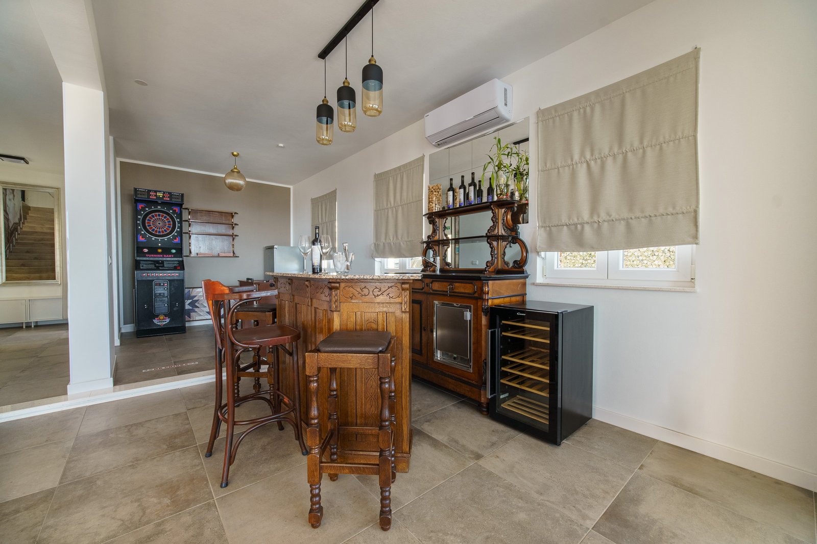 Carved wooden bar with stools and a wine fridge beside an electronic dartboard.