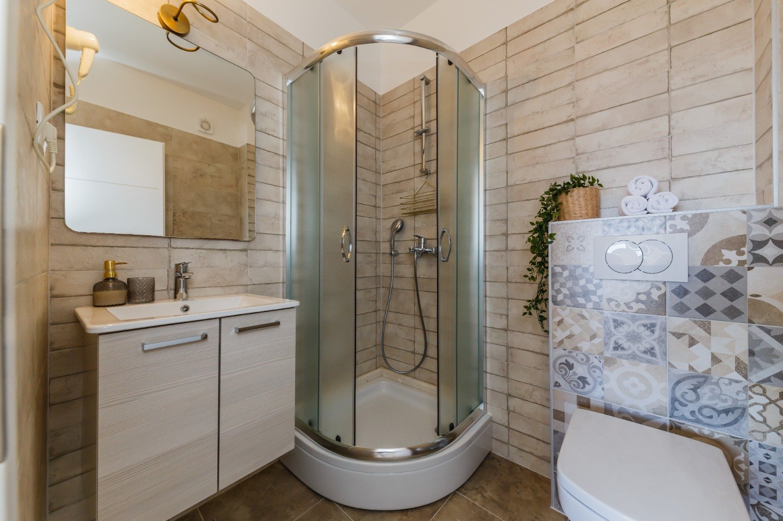 Bathroom with a curved glass shower enclosure, white vanity and patterned tiles beneath folded towels.