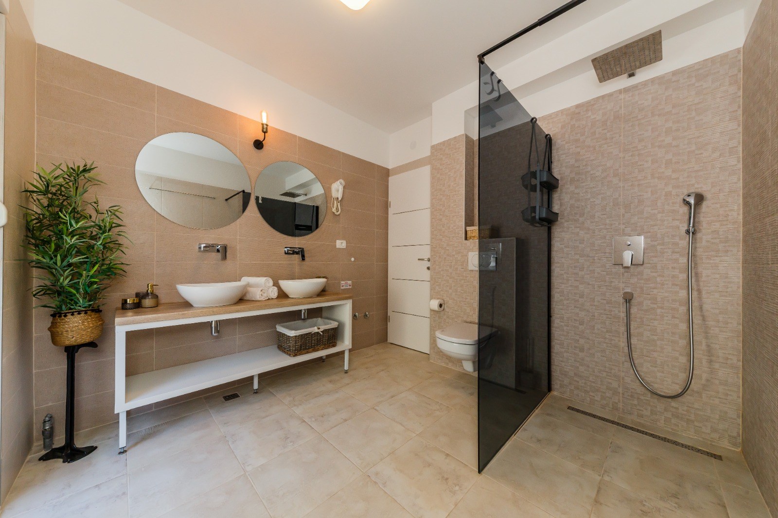 Bathroom with twin basins, circular mirrors and a glass-screened walk-in shower.